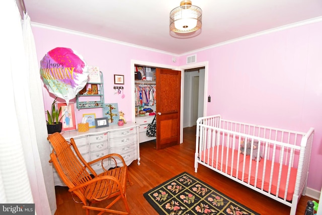 bedroom with a closet, a nursery area, wood-type flooring, and crown molding