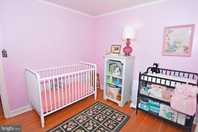 bedroom featuring crown molding, hardwood / wood-style flooring, and a crib