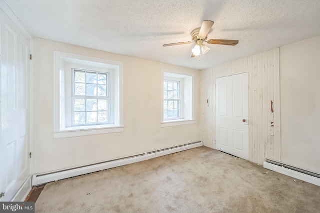 carpeted empty room featuring ceiling fan, baseboard heating, a textured ceiling, and plenty of natural light