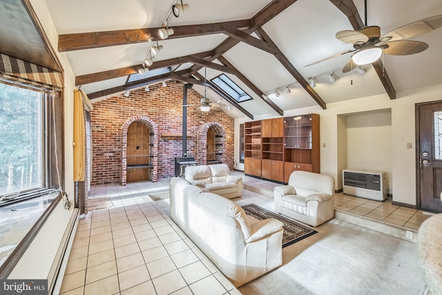 unfurnished living room with heating unit, rail lighting, vaulted ceiling with skylight, a wood stove, and brick wall