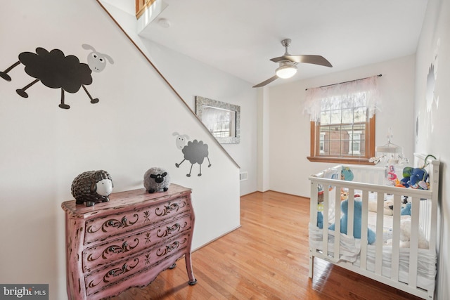 bedroom with hardwood / wood-style flooring, ceiling fan, and a nursery area