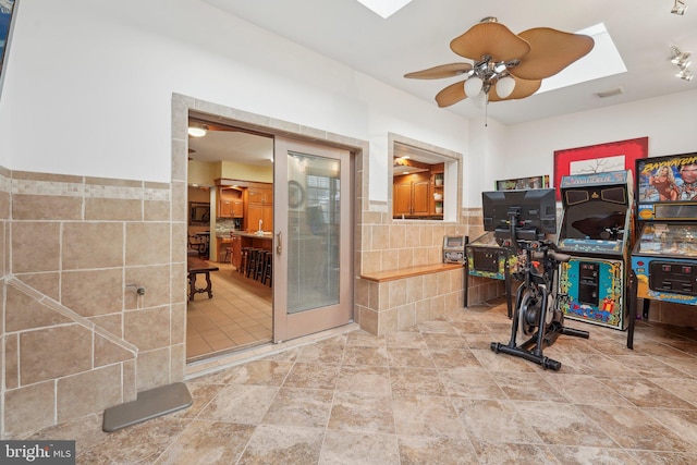 workout room featuring a skylight, ceiling fan, and tile walls