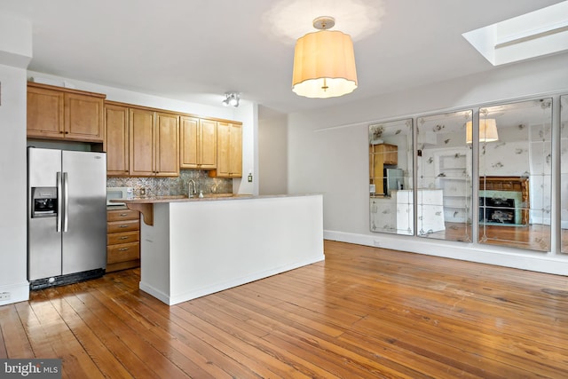 kitchen featuring a skylight, stainless steel fridge, light hardwood / wood-style flooring, backsplash, and a kitchen breakfast bar