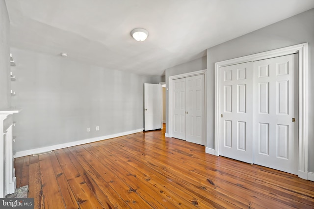 unfurnished bedroom with two closets and wood-type flooring