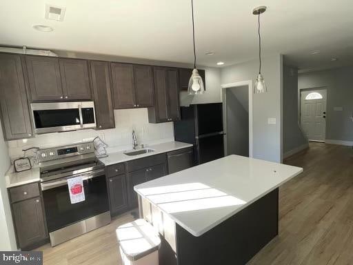 kitchen featuring black appliances, hanging light fixtures, sink, and light hardwood / wood-style flooring