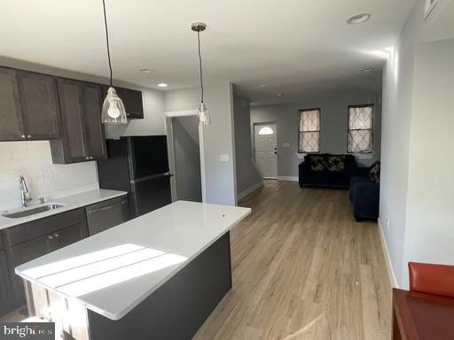 kitchen with sink, a kitchen island, dark brown cabinets, black appliances, and light wood-type flooring