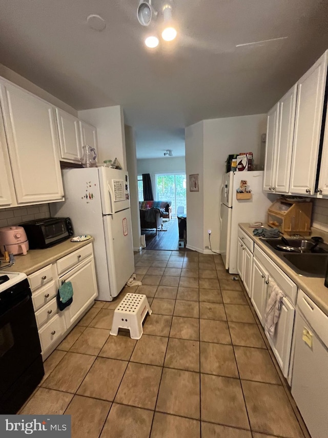 kitchen with tasteful backsplash, white cabinetry, sink, tile patterned flooring, and white appliances