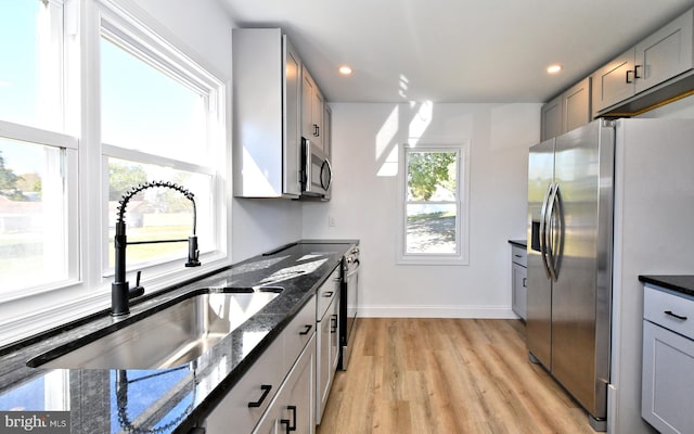 kitchen featuring dark stone counters, stainless steel appliances, plenty of natural light, and light wood-type flooring