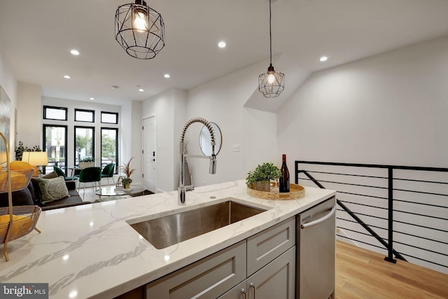 kitchen featuring light stone counters, hanging light fixtures, sink, stainless steel dishwasher, and light hardwood / wood-style flooring