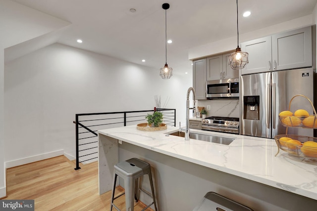 kitchen featuring gray cabinetry, pendant lighting, light hardwood / wood-style flooring, light stone counters, and stainless steel appliances