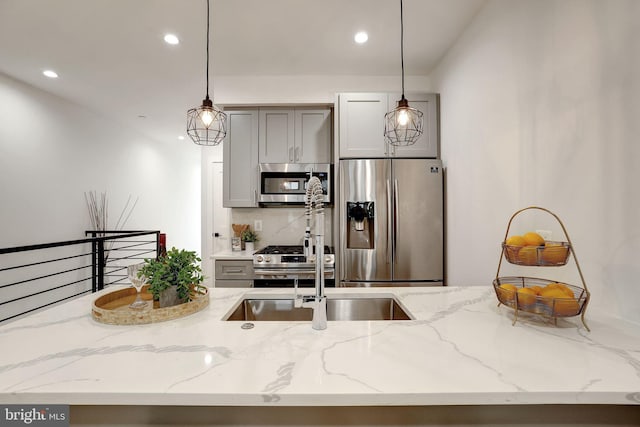 kitchen featuring light stone countertops, stainless steel appliances, gray cabinetry, sink, and hanging light fixtures