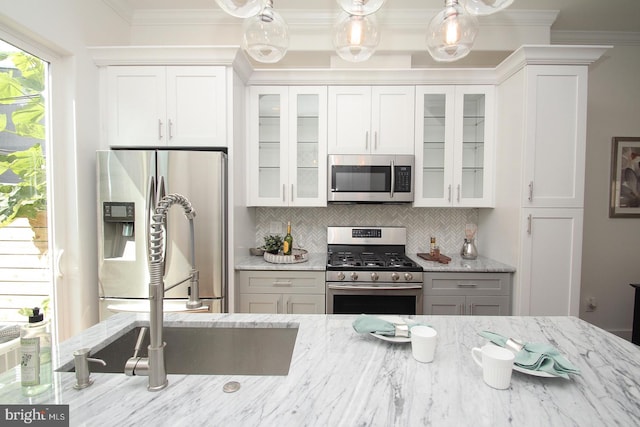 kitchen with light stone counters, stainless steel appliances, white cabinets, ornamental molding, and backsplash