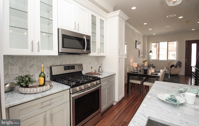 kitchen featuring light stone counters, stainless steel appliances, white cabinets, dark wood-type flooring, and backsplash