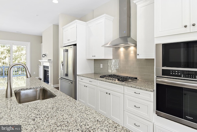 kitchen featuring light stone counters, sink, wall chimney range hood, white cabinetry, and stainless steel appliances