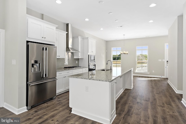 kitchen featuring an island with sink, stainless steel appliances, wall chimney range hood, and white cabinetry