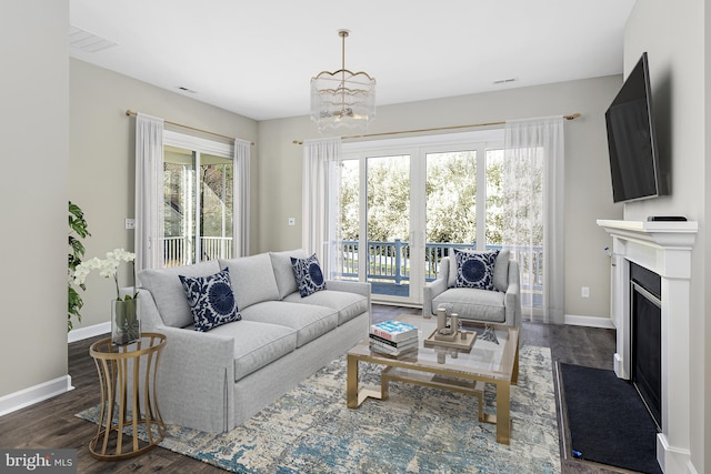living area with dark wood-style flooring, baseboards, a notable chandelier, and a fireplace