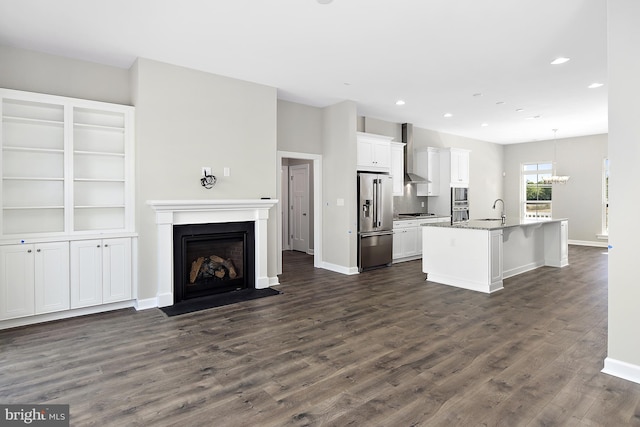 kitchen with open floor plan, white cabinetry, wall chimney exhaust hood, stainless steel appliances, and a sink