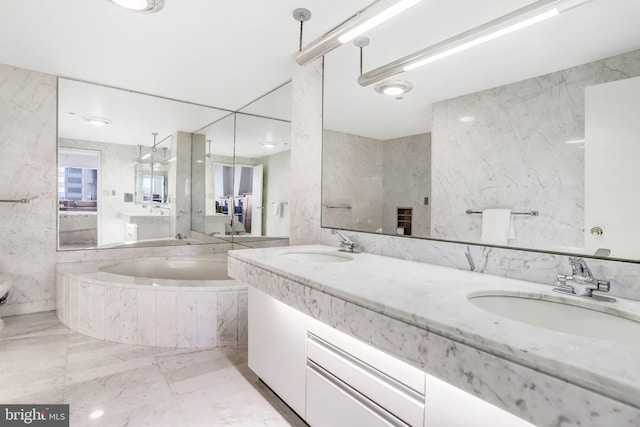 bathroom with marble finish floor, a bath, double vanity, and a sink