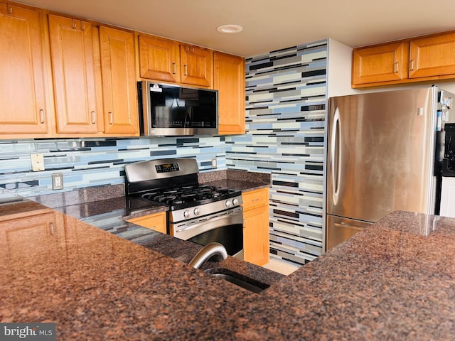 kitchen featuring tasteful backsplash, appliances with stainless steel finishes, sink, and dark stone countertops