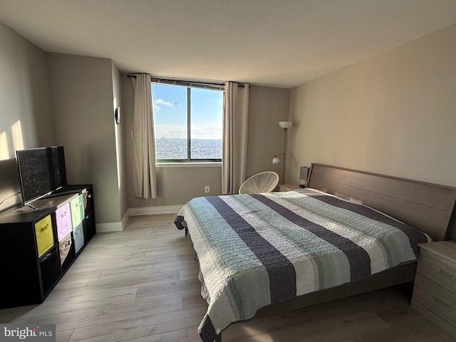 bedroom featuring a water view, a textured ceiling, and light hardwood / wood-style flooring