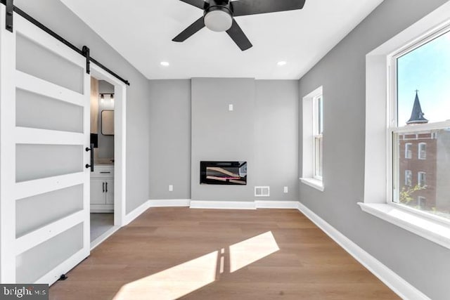 unfurnished living room with ceiling fan, a barn door, and light hardwood / wood-style floors