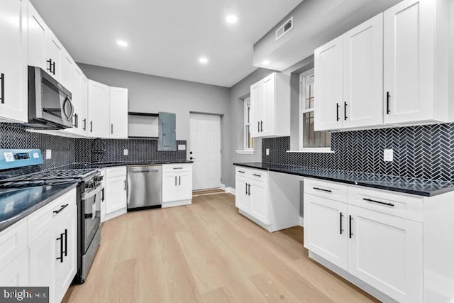 kitchen with decorative backsplash, white cabinets, stainless steel appliances, and light hardwood / wood-style flooring