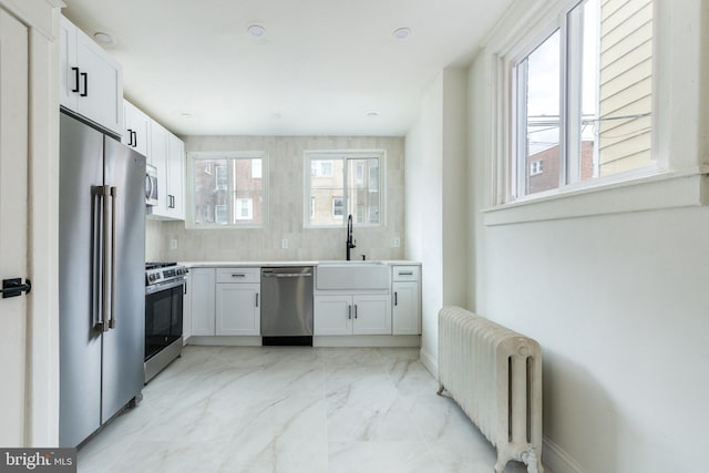 kitchen featuring white cabinets, sink, radiator heating unit, and stainless steel appliances