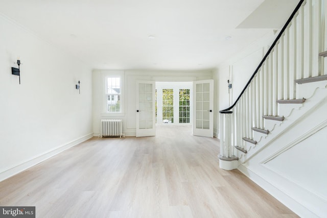 foyer entrance featuring light hardwood / wood-style floors, crown molding, radiator, and french doors