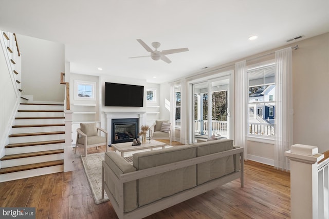 living area featuring a healthy amount of sunlight, stairway, wood finished floors, and a glass covered fireplace