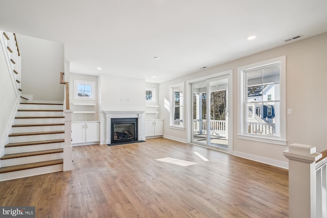 unfurnished living room with a healthy amount of sunlight, light wood finished floors, a fireplace with flush hearth, and visible vents