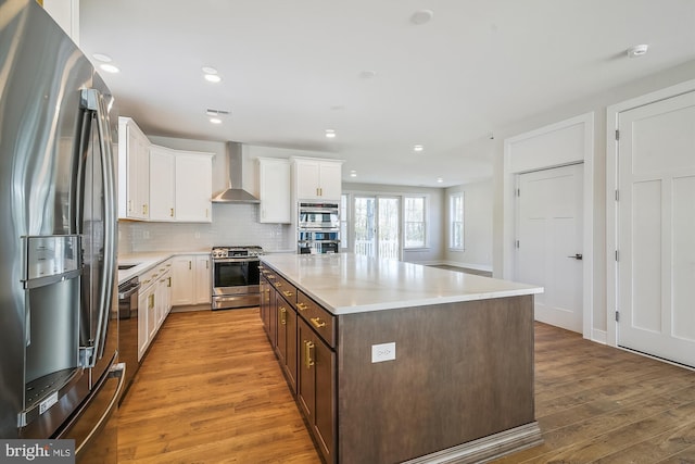 kitchen featuring tasteful backsplash, appliances with stainless steel finishes, light wood-style floors, white cabinets, and wall chimney range hood