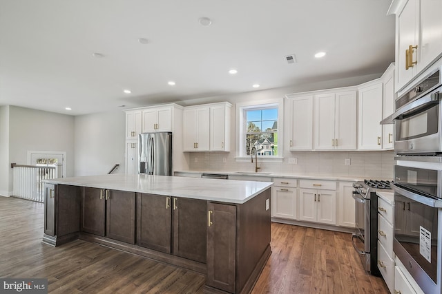 kitchen featuring appliances with stainless steel finishes, white cabinets, a sink, and a center island