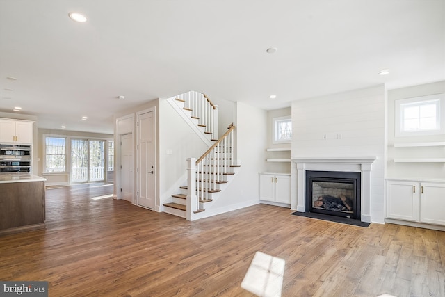 unfurnished living room with plenty of natural light, stairway, wood finished floors, and a fireplace with flush hearth