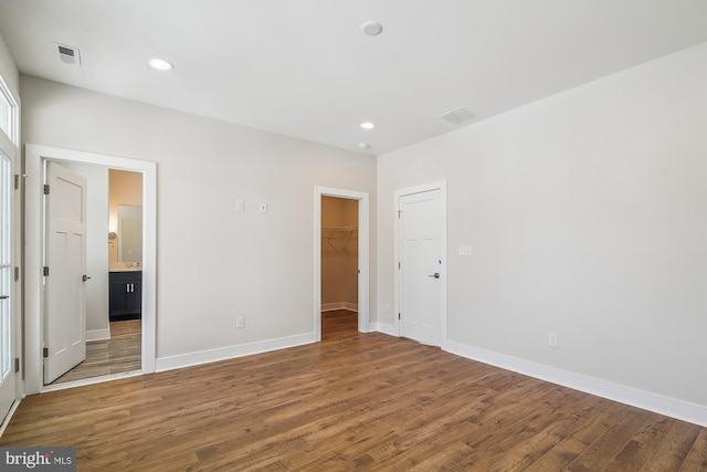 unfurnished bedroom featuring a walk in closet, recessed lighting, visible vents, wood finished floors, and baseboards