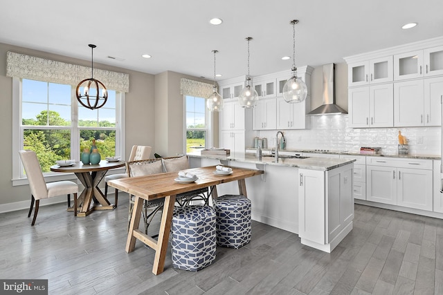 kitchen with a center island with sink, pendant lighting, wall chimney exhaust hood, and a healthy amount of sunlight