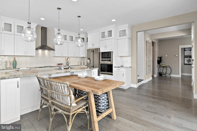 kitchen with wall chimney range hood, white cabinets, appliances with stainless steel finishes, and light stone counters