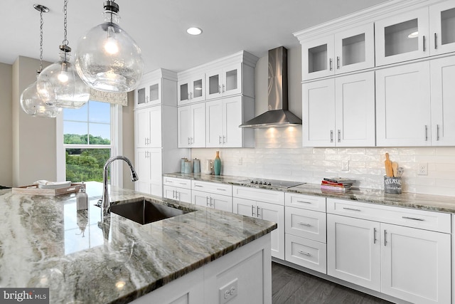 kitchen featuring hanging light fixtures, wall chimney exhaust hood, white cabinetry, and sink