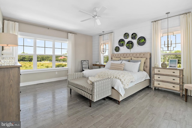 bedroom with ceiling fan with notable chandelier, hardwood / wood-style floors, and multiple windows