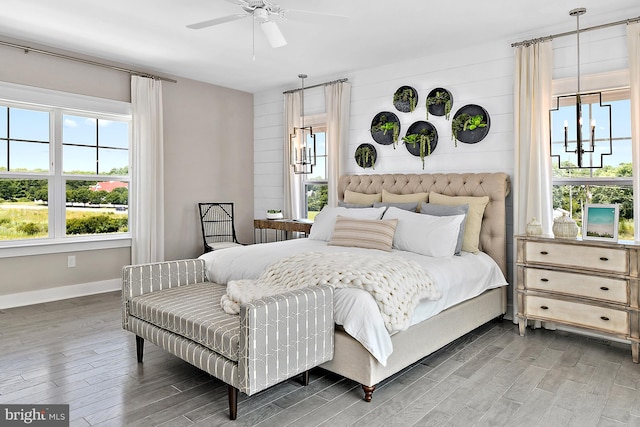 bedroom with ceiling fan with notable chandelier, wooden walls, hardwood / wood-style flooring, and multiple windows