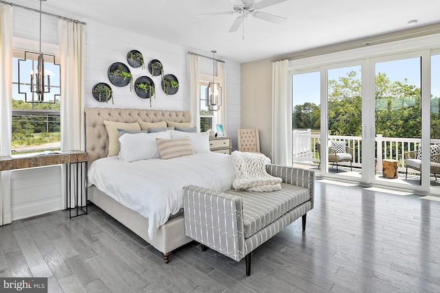 bedroom featuring ceiling fan with notable chandelier, wood walls, access to outside, and hardwood / wood-style floors