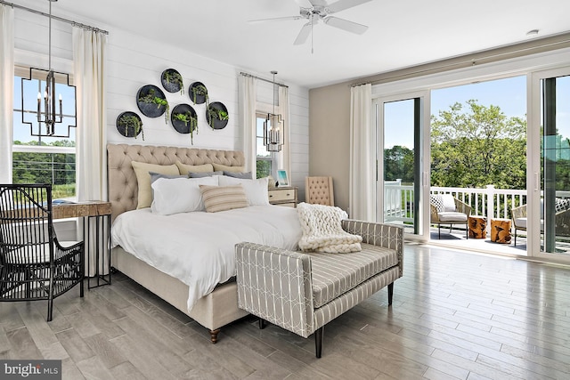 bedroom with access to outside, ceiling fan with notable chandelier, wooden walls, and wood-type flooring