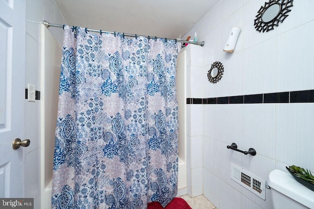 bathroom with tile walls, shower / bath combo with shower curtain, and toilet