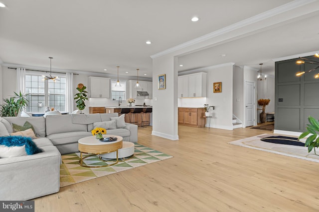 living room with crown molding, a chandelier, and light wood-type flooring