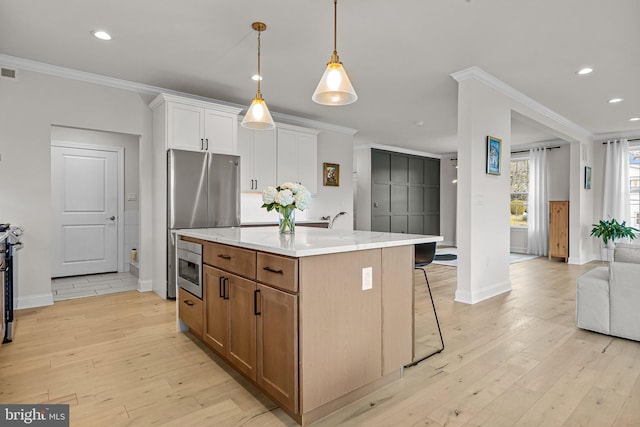 kitchen with a center island with sink, appliances with stainless steel finishes, white cabinetry, light hardwood / wood-style flooring, and ornamental molding