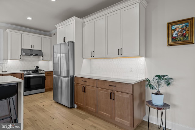 kitchen with appliances with stainless steel finishes, backsplash, white cabinetry, ornamental molding, and light hardwood / wood-style flooring