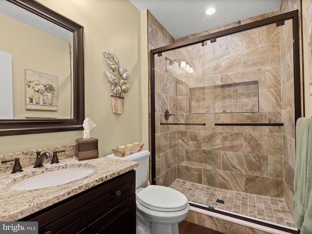 bathroom featuring a shower with door, vanity, and toilet