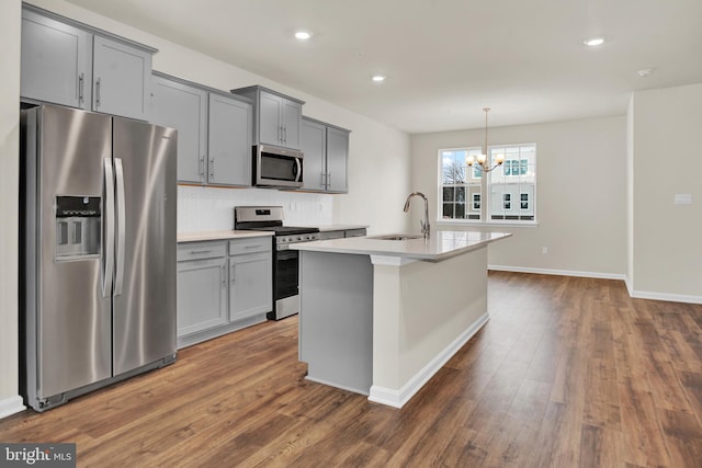 kitchen featuring appliances with stainless steel finishes, dark hardwood / wood-style floors, an island with sink, sink, and hanging light fixtures