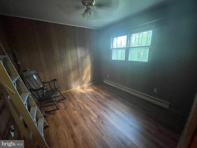 unfurnished room with ceiling fan, wood walls, dark wood-type flooring, and a baseboard heating unit