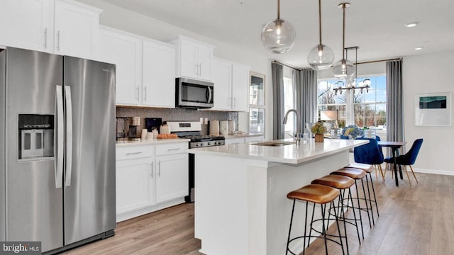 kitchen with a kitchen island with sink, stainless steel appliances, sink, light wood-type flooring, and white cabinets