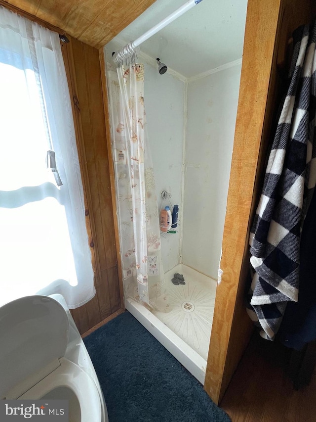 bathroom with wooden walls, crown molding, and walk in shower